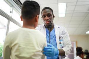 Black skin doctor checking up kid body in clinic. photo