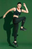 hermosa fuerte feliz alegre joven mujer deportiva asiática hace ejercicios aislados sobre fondo verde. chica fitness en ropa deportiva posando en el interior. movimiento, fuerza y motivación. foto