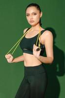 Beautiful strong happy cheerful young Asian sports woman does exercises isolated on green background. Fitness girl in sportswear posing indoors. Movement, Strength and motivation. photo