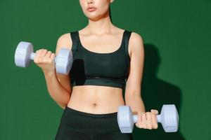 crop close up body of young Asian sports woman does exercises isolated on green background. Fitness girl in sportswear posing indoors. Movement, Strength and motivation. photo