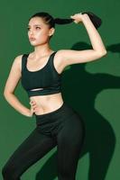 hermosa fuerte feliz alegre joven mujer deportiva asiática hace ejercicios aislados sobre fondo verde. chica fitness en ropa deportiva posando en el interior. movimiento, fuerza y motivación.