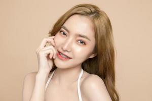 Cute young Asian woman wearing braces is feeling happy with clean fresh skin isolated over cream background. Plastic surgery Face care, Facial treatment, Cosmetology, beauty and spa, Women portrait.