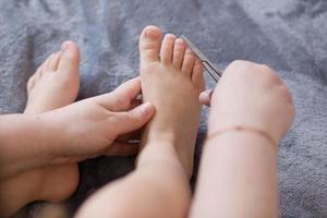 Mother cuts the child's toenails. Close-up. Mother cutting nails on feet of her kid photo