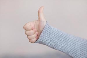 close-up photo of a child's hand of a girl showing a thumbs up sign on a light background.Thumbs up. A child's hand shows the like