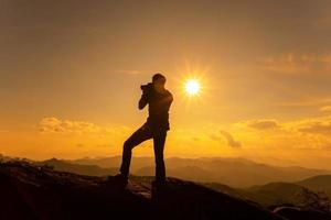 silueta de un fotógrafo tomando fotos de un hermoso paisaje en la alta montaña durante el momento del atardecer.