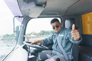 conductor de camión profesional, hombre adulto asiático con gafas de sol sonríe y levanta la mano. el joven trabajador confía en la seguridad del negocio de transporte y entrega durante mucho tiempo. foto