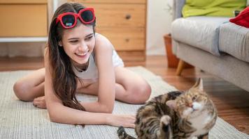 smiling young woman playing with cat in room. photo