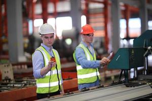 Men industrial engineer wearing a safety helmet while standing in a heavy industrial factory. The Maintenance looking of working at industrial machinery and check security system setup in factory. photo