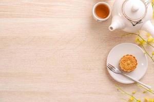 Tasty moon cake for Mid-Autumn festival on bright wooden table, concept of festive afternoon tea decorated with yellow flowers, top view, flat lay. photo