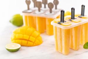 Fresh mango fruit popsicle ice in the plastic shaping box on bright marble table. Summer mood concept product design, close up. photo