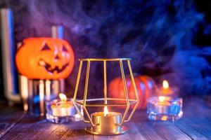 concepto de halloween, linterna de calabaza naranja y velas en una mesa de madera oscura con humo azul-naranja alrededor del fondo, truco o trato, cerrar