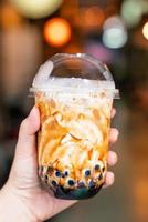 Young girl is holding and showing a cup of brown sugar flavored tapioca pearl bubble milk tea in night market of Taiwan background, close up, bokeh photo