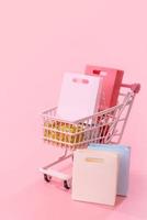 Annual sale shopping season concept - mini red shop cart trolley full of paper bag gift isolated on pale pink background, blank copy space, close up photo