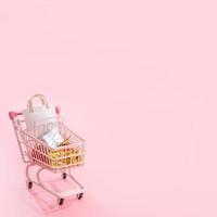 Annual sale shopping season concept - mini red shop cart trolley full of paper bag gift isolated on pale pink background, blank copy space, close up photo