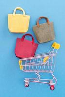 Abstract design element, annual sale, shopping season concept, mini yellow cart with colorful paper bag on pastel blue background, top view, flat lay photo