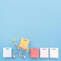 Abstract design element, annual sale, shopping season concept, mini yellow cart with colorful paper bag on pastel blue background, top view, flat lay photo