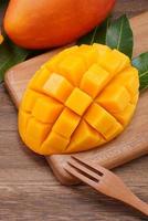 Fresh mango, beautiful chopped fruit with green leaves on dark wooden table background. Tropical fruit design concept. Flat lay. Top view. Copy space photo