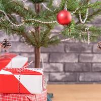 árbol de navidad decorado con hermosos regalos rojos y blancos envueltos en casa con pared de ladrillo negro, concepto de diseño festivo, primer plano. foto