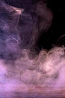 Conceptual image of multi-colored smoke isolated on dark black background and wooden table. photo