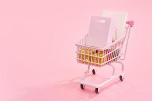 Annual sale shopping season concept - mini pink shop cart trolley full of paper bag gift isolated on pale pink background, blank copy space, close up photo