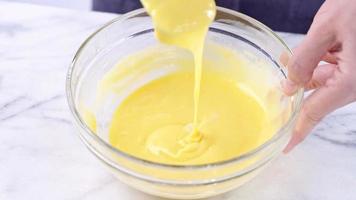 Mixing egg yolk into cake batter with green rubber spatula mixer tool stirring until smooth and blend well in a glass bowl, close up, lifestyle photo