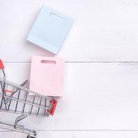 Abstract design element,annual sale,shopping season concept,mini cart with colorful paper bag on white wooden table background,top view,flat lay photo