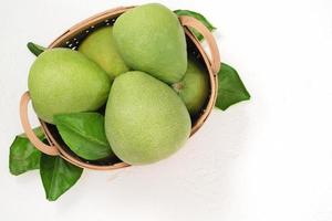 Fresh pomelo, pummelo, grapefruit, shaddock on white cement background in bamboo basket. Autumn seasonal fruit, top view, flat lay, tabletop shot. photo