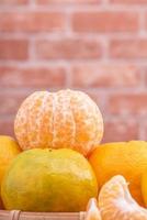 Peeled tangerines in a bamboo sieve basket on dark wooden table with red brick wall background, Chinese lunar new year fruit design concept, close up. photo