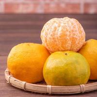 Peeled tangerines in a bamboo sieve basket on dark wooden table with red brick wall background, Chinese lunar new year fruit design concept, close up. photo