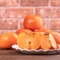 Fresh beautiful sliced sweet persimmon kaki on dark wooden table with red brick wall background, Chinese lunar new year fruit design concept, close up. photo