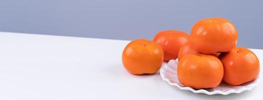 Fresh beautiful sliced sweet persimmon kaki isolated on white kitchen table with gray blue background, Chinese lunar new year design concept, close up. photo