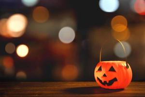 concepto de halloween - linterna de calabaza de plástico naranja sobre una mesa de madera oscura con una luz brillante borrosa en el fondo, truco o trato, de cerca.
