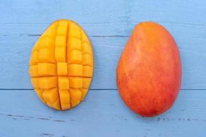 Fresh mango - beautiful chopped fruit with green leaves on bright blue timber background. Tropical fruit design concept. Flat lay. Top view. Copy space photo