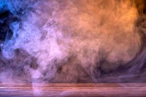 Conceptual image of multi-colored smoke isolated on dark black background and wooden table. photo