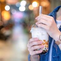 Young girl in denim jacket is drinking brown sugar flavored tapioca pearl bubble milk tea with glass straw in night market of Taiwan, close up, bokeh photo