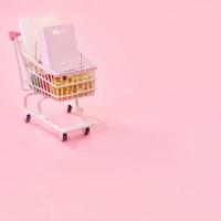 Annual sale shopping season concept - mini red shop cart trolley full of paper bag gift isolated on pale pink background, blank copy space, close up photo