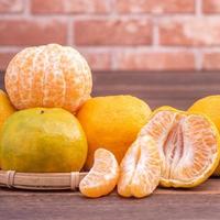 Peeled tangerines in a bamboo sieve basket on dark wooden table with red brick wall background, Chinese lunar new year fruit design concept, close up. photo