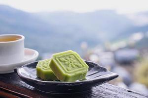Delicioso pastel de frijol mungo verde con plato de té negro en una barandilla de madera de una casa de té en taiwán con un hermoso paisaje de fondo, de cerca. foto