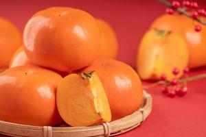 Fresh beautiful sliced sweet persimmon kaki isolated on red table background and bamboo sieve, Chinese lunar new year design concept, close up. photo