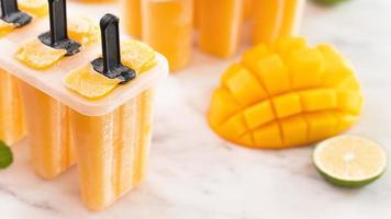 Fresh mango fruit popsicle ice in the plastic shaping box on bright marble table. Summer mood concept product design, close up. photo