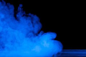 Conceptual image of blue smoke isolated on dark black background and wooden table. photo