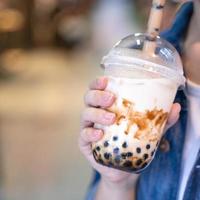 Young girl in denim jacket is drinking brown sugar flavored tapioca pearl bubble milk tea with glass straw in night market of Taiwan, close up, bokeh photo