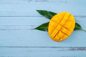 Fresh mango, beautiful chopped fruit with green leaves on dark wooden table background. Tropical fruit design concept. Flat lay. Top view. Copy space photo