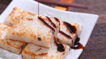 Pouring black soy sauce on ready-to-eat delicious turnip cake, Chinese traditional local dish radish cake in restaurant, close up, copy space. photo