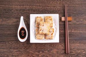 Delicious turnip cake, Chinese traditional local radish cake in restaurant with soy sauce and chopsticks, close up, copy space, top view, flat lay. photo