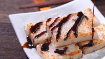 Verter salsa de soja negra en un delicioso pastel de nabo listo para comer, pastel de rábano local tradicional chino en el restaurante, primer plano, espacio para copiar. foto