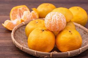 Mandarina fresca y hermosa de color naranja en un tamiz de bambú sobre una mesa de madera oscura. fruta estacional y tradicional del año nuevo lunar chino, de cerca.