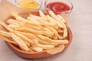 Golden yummy deep French fries on kraft baking sheet paper and serving tray to eat with ketchup and yellow mustard, close up, lifestyle. photo