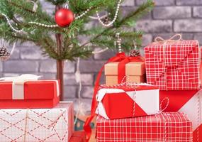 árbol de navidad decorado con hermosos regalos rojos y blancos envueltos en casa con pared de ladrillo negro, concepto de diseño festivo, primer plano.