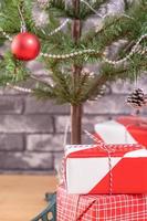 Decorated Christmas tree with wrapped beautiful red and white gifts at home with black brick wall, festive design concept, close up. photo